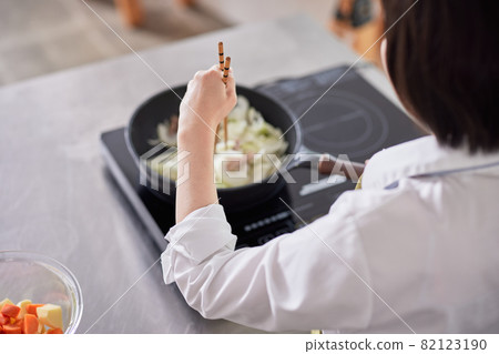 A young woman in an apron cooking in the kitchen 82123190