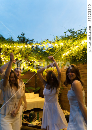 Dancing at a summer party. Fun and joy of friends outside, bottles of beer. A group of people dancing to music in the yard Dancing at a summer party. Fun and joy of friends outside, bottles of beer. A group of people dancing to music in the yard 82123340