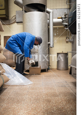 Mid adult man in uniform setting up roasting machine Mid adult man in uniform setting up roasting machine 82123871