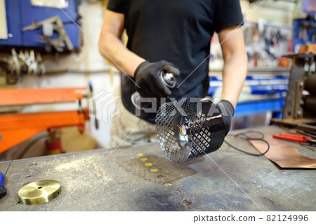 Metalwork craftsman making handmade lamp at workshop. Man worker painting of lampshade. Diy. Small local business. 82124996