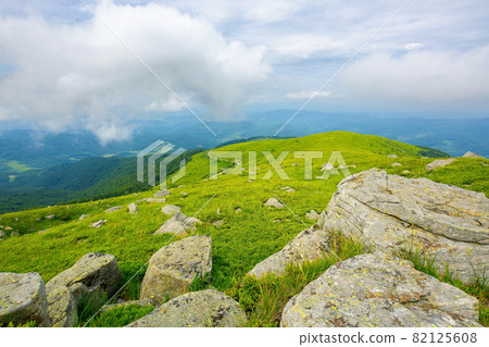 view from runa mountain. huge stones on the grassy slopes. summer landscape of carpathian mountains. bieszczady and vihorlat ridge in the distance beneath a sky low clouds view from runa mountain. huge stones on the grassy slopes. summer landscape of carpathian mountains. bieszczady and vihorlat ridge in the distance beneath a sky low clouds 82125608