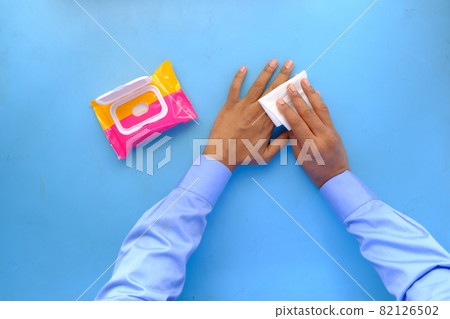 man disinfecting his hands with a wet wipe on blue background  82126502