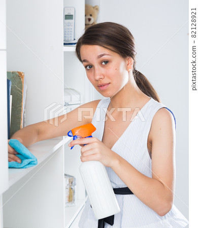 Teenager is cleaning dust from shelves 82128921