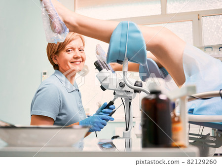 Smiling gynecologist in sterile gloves doing colposcopy examination with colposcope in gynecological cabinet. Woman patient laying in the chair. Concept of gynecology, medicine and female health. Smiling gynecologist in sterile gloves doing colposcopy examination with colposcope in gynecological cabinet. Woman patient laying in the chair. Concept of gynecology, medicine and female health. 82129260