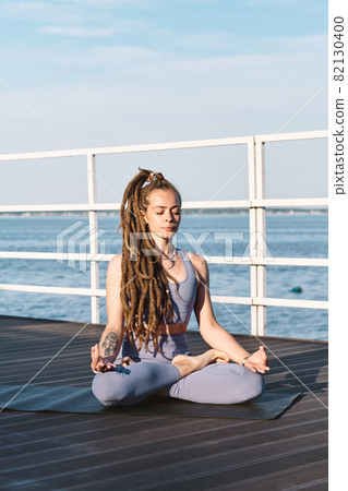 Contemporary sportswoman sitting in pose of lotus Contemporary sportswoman sitting in pose of lotus 82130400