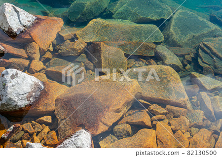 Coastal stones partially underneath the clear fresh water of the lake 82130500