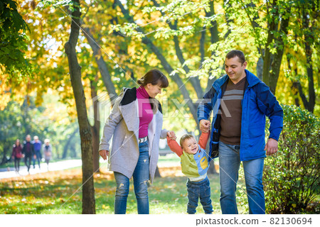 Beautiful young family on a walk in autumn forest on maple yellow trees background. Father and mother hold son on hands. Happy family leisure together concept 82130694