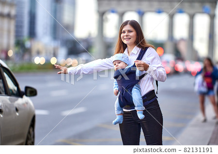 Woman with child in baby sling stops taxi on busy city street. Woman with child in baby sling stops taxi on busy city street. 82131191