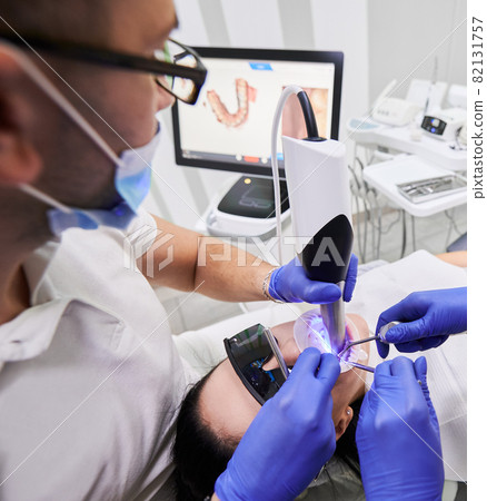 Close up of dentist and assistant using dental intraoral scanner while examining patient teeth in dental office. Intraoral scanning with modern scanning machine. Concept of digital dentistry Close up of dentist and assistant using dental intraoral scanner while examining patient teeth in dental office. Intraoral scanning with modern scanning machine. Concept of digital dentistry 82131757