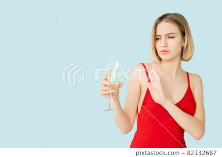 Stop drink. Skeptic woman. Party doubt. Festive celebration. Advertising background. Protesting lady red dress refusing glass of champagne isolated blue copy space. 82132687