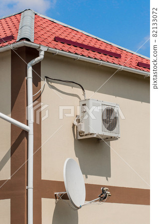 Air conditioner and satellite dish on the wall of a modern house next roof on the street outdoor 82133072