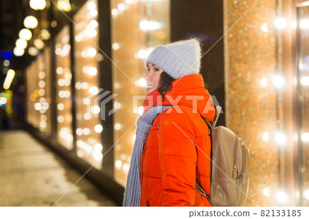 Happy funny young woman with winter clothes background evening city lights illumination. Christmas and winter holidays concept. 82133185