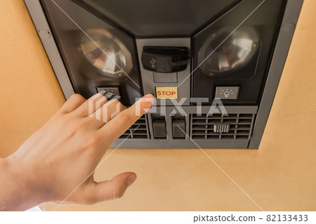 The guy's hand points his finger at the stop button of the air conditioning system in the ceiling of the tourist bus The guy's hand points his finger at the stop button of the air conditioning system in the ceiling of the tourist bus 82133433