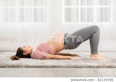 Pregnant Asian young woman breathing meditation with yoga Half Bridge pose,Yoga meditation of young healthy pregnant woman relax and comfortable at white cozy home,Yoga Exercise for Wellness Concept 82134766