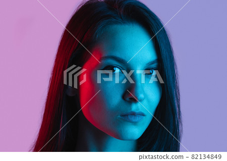 Close-up portrait of young beautiful caucasian girl posing isolated over gradient pink purple background in neon lights 82134849