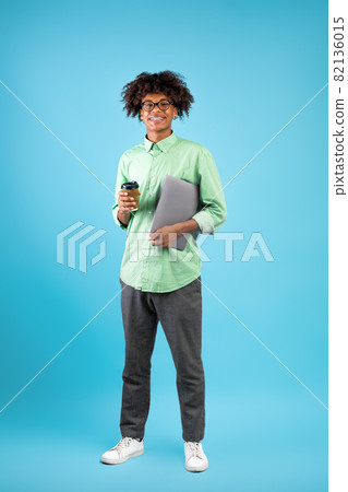 Modern student. Happy black guy with laptop computer and takeaway coffee posing to camera on blue background Modern student. Happy black guy with laptop computer and takeaway coffee posing to camera on blue background 82136015