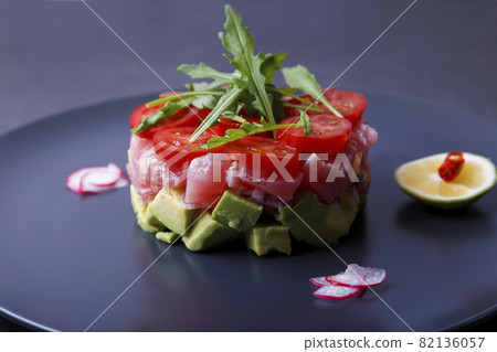 Fresh tuna tartare with avocado, arugula, cherry tomatoes, radish, chili and lime. Traditional cold appetizer of French cuisine. Close-up, selective focus. Fresh tuna tartare with avocado, arugula, cherry tomatoes, radish, chili and lime. Traditional cold appetizer of French cuisine. Close-up, selective focus. 82136057