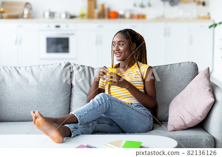 Relaxed african-american young woman chilling on couch with coffee mug Relaxed african-american young woman chilling on couch with coffee mug 82136126