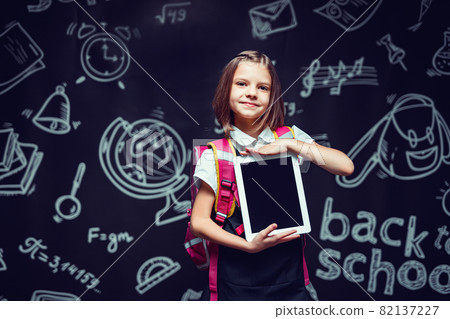 Cute schoolgirl preparing to go to school with backpack showing the tablet. Back to school concept Cute schoolgirl preparing to go to school with backpack showing the tablet. Back to school concept 82137227
