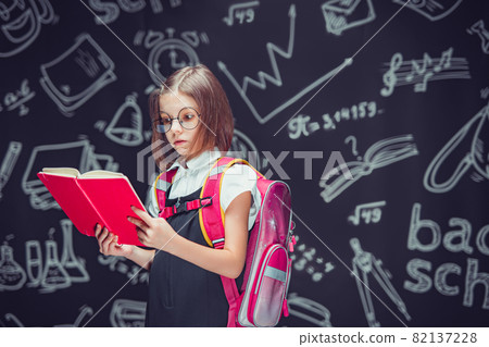 Serious pupil in glasses preparing to go to school with backpack reading book. Back to school Serious pupil in glasses preparing to go to school with backpack reading book. Back to school 82137228