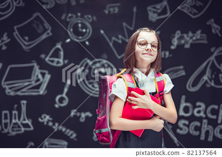 Happy schoolgirl in glasses preparing to go to school with backpack holding book. Back to school Happy schoolgirl in glasses preparing to go to school with backpack holding book. Back to school 82137564