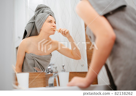 Woman with a towel on her head brushes her teeth. 82138262