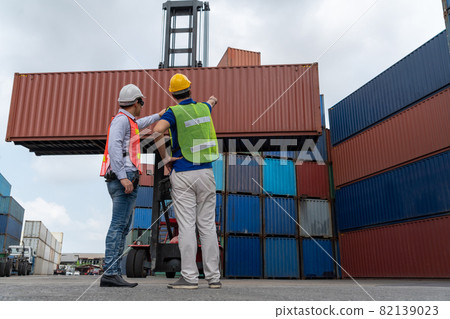 Industrial worker works with co-worker at overseas shipping container yard Industrial worker works with co-worker at overseas shipping container yard 82139023