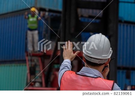 Industrial worker works with co-worker at overseas shipping container yard Industrial worker works with co-worker at overseas shipping container yard 82139061