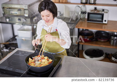 一個穿著圍裙在廚房裡做咖哩的年輕女人 一個穿著圍裙在廚房裡做咖哩的年輕女人 82139736