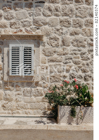 Old window with wooden shutters on yellow stucco wall and copy space Old Shutter windows with a flowers. Montenegro. Mediterranean. 82140374