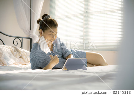 woman and face mask reading massege with relaxing on mattress in messed up bedroom woman and face mask reading massege with relaxing on mattress in messed up bedroom 82145318