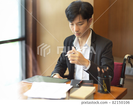 Young smart businessman in wheelchair working at his desk 82150106
