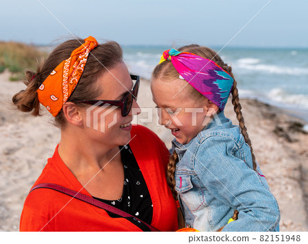 Cheerful mother and daughter smiling walking on sea beach. Happy family. Cute little child playing rainbow pop it toy 82151948