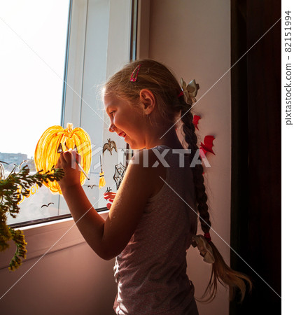 Child painting pumpkin on window preparing to celebrate Halloween. Little girl decorates her room autumn holiday at home 82151994