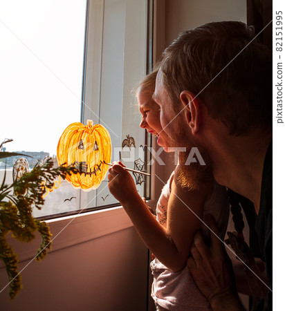 Child with father painting pumpkin on window preparing to Halloween Little girl with dad drawing decorating room Child with father painting pumpkin on window preparing to Halloween Little girl with dad drawing decorating room 82151995