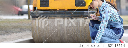 Woman examines asphalt pavement in front of asphalt paver Woman examines asphalt pavement in front of asphalt paver 82152514