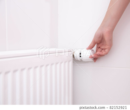 A woman's hand holds the heating thermostat handle. Heating service cost concept, utility price increase. Copy space for text 82152921