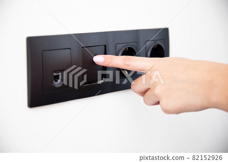 The girl presses the button of the broken electrical switch combined with the socket. Electric shock concept with faulty equipment, close-up 82152926