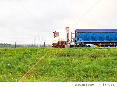 The tonar semitrailer semitrailer for transporting natural resources travels along the road in summer. Overcast sky, copy space for text The tonar semitrailer semitrailer for transporting natural resources travels along the road in summer. Overcast sky, copy space for text 82152943