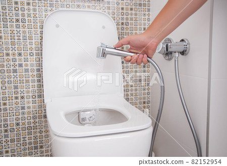A man holds a hygienic shower against the background of the toilet bowl. Intimate body care and hygiene concept, close-up 82152954