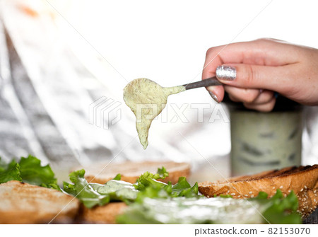 The girl puts sauce on homemade burgers with a spoon. Cooking delicious fast food at home, close-up 82153070