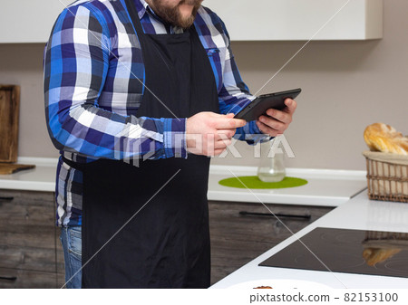 A man in the kitchen is watching a recipe for cooking a dish on a tablet on the Internet, background A man in the kitchen is watching a recipe for cooking a dish on a tablet on the Internet, background 82153100
