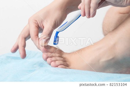 A man holds a razor near his toes where hair grows. Concept for shaving hair on legs and toes, epilation, cosmetic A man holds a razor near his toes where hair grows. Concept for shaving hair on legs and toes, epilation, cosmetic 82153104