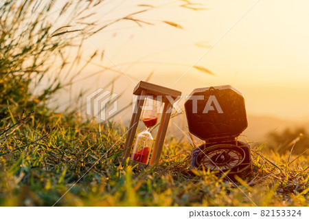 Hourglass and compass with sunrise in the morning at mountain Hourglass and compass with sunrise in the morning at mountain 82153324