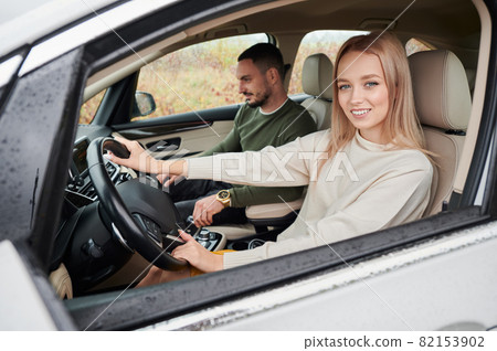 Happy man and woman traveling in car. Young couple sitting on front passenger seats. Portrait of beautiful smiling woman driving comfortable automobile. 82153902