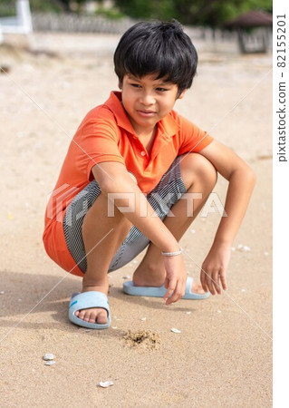 Portrait Asian boys wearing an orange shirt sitting on the beach 82155201
