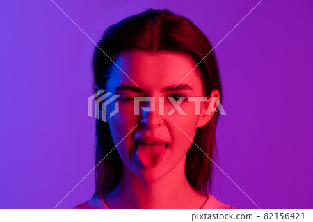 Close-up portrait of young girl making faces isolated on purple, lilac color studio background. Concept of human emotions, facial expression, cosmetics, youth Close-up portrait of young girl making faces isolated on purple, lilac color studio background. Concept of human emotions, facial expression, cosmetics, youth 82156421