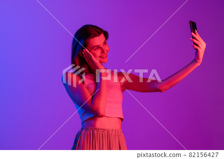 One young Caucasian girl using phone isolated on purple, lilac color studio background. Concept of human emotions, facial expression, cosmetics, youth One young Caucasian girl using phone isolated on purple, lilac color studio background. Concept of human emotions, facial expression, cosmetics, youth 82156427