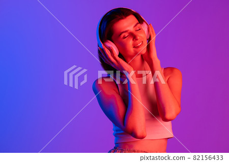 Half-length portrait of young girl isolated on purple, lilac color studio background in neon light. Concept of human emotions, facial expression, cosmetics, youth 82156433