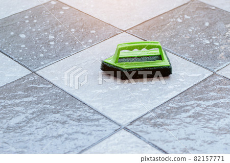 Close up a green plastic brush for scrubbing and cleaning floors placed on a wet tiled floor. 82157771